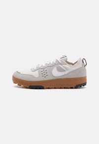 Sneaker grigie chiare con tomaia in suede e tela, logo bianco e suola in gomma naturale. Presentano accenti e lacci neri in contrasto.