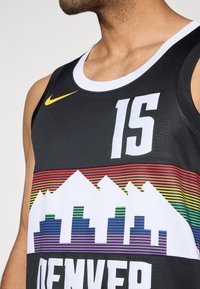 Mustat koripallopaidat, joissa on valkoinen kaula-aukko, rohkea valkoinen numero "15" ja värikäs grafiikka vuorista sekä kaupunkitaivasta alaosassa.