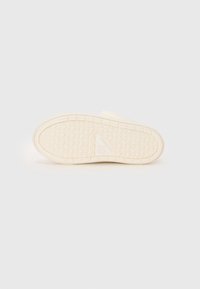 Schuhsohle aus hellem beigefarbenem Gummi mit strukturiertem Grifffmuster, ausgestattet mit einem Dreieckslogo und minimalistischem Design mit abgerundeten Kanten.