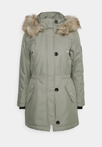 Parka imbottita di colore verde oliva con cappuccio in pelliccia sintetica removibile. Presenta una vita con cordino, due tasche frontali e chiusure a bottoni neri.