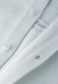 Gilet tricoté bleu clair avec des boutons ronds et transparents, et un motif texturé détaillé près de l'encolure. Comprend un petit détail de trou.