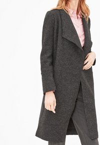 Dark grey wool coat with a notched lapel, long sleeves, and an open front. Worn over a pink shirt and tailored trousers.