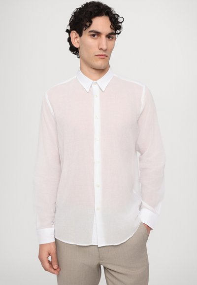 Camisa blanca, ligera, con mangas largas, cierre de botones en la parte delantera y un cuello clásico. Tela texturizada con un aspecto ligeramente translúcido.