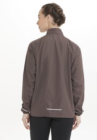 Brun lättviktsjacka med hög krage, elastiska manschetter och en reflekterande rand bak, med en slät yta och minimalistisk design.