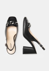 Tacchi slingback in pelle nera con punta quadrata, tacco a blocco spesso e dettaglio in catena argento sulla parte anteriore. Texture liscia e design classico.
