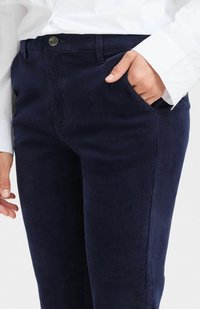 Pantaloni in corduroy blu navy con una texture liscia, taglio slim, tasche laterali e chiusura frontale con bottone, abbinati a una camicia bianca a maniche lunghe.