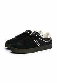 Para czarnych niskich sneakersów z białymi akcentami, marki "Tommy Jeans", z zapięciem na sznurówki i wyściełanym białym wnętrzem.