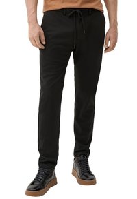 Zwarte joggings met elastische tailleband en trekkoord, met een zachte textuur en een tapered fit. Gecombineerd met zwarte sneakers en tan accenten.