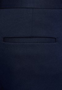 Tessuto blu navy con una trama liscia che presenta un design con una singola tasca a filetto. Vista ravvicinata che mette in risalto i dettagli del materiale e delle cuciture.