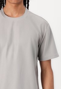 Lysegrå kortærmet t-shirt lavet af ribbet stof. Har en rund halsudskæring og diskrete sømdetaljer langs sømmene.