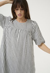 Juodai balta dryžuota suknelė su trumpomis pūkuotomis rankovėmis, tekstūruotas audinys, laisvas siluetas, turinti surinktos detalės prie kaklo.