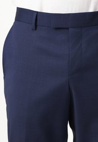 Marineblaue maßgeschneiderte Hose aus glattem, strukturiertem Stoff. Verfügt über einen normalen Bund und eine Seitentasche. Schlichtes, minimalistisches Design.