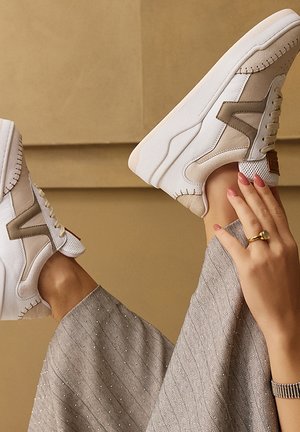 White and beige sneakers with textured fabric, lace-up design, and contrasting side accents. Smooth sole, visible stitching details.
