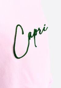 T-shirt in tessuto rosa con testo ricamato in verde scuro che scrive "Capri", con una texture liscia e un design a vestibilità rilassata.