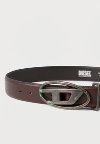 Rjav usnjen pas z velikim ovalnim kovinskim zaponkom z zrelim zelenkastim odtenkom. Vključno z več luknjami za prilagajanje vzdolž traku.