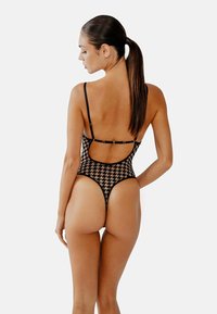 Svart baddräkt med houndstooth-mönster, öppen ryggdesign, tunna axelband och höga ben, vilket framhäver en åtsittande stil och slät textur.