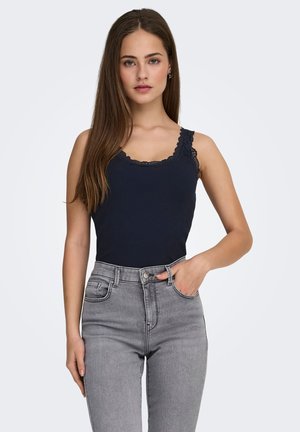 Navy ribbed tank top with lace trim, paired with high-waisted gray jeans. The tank features adjustable straps and a fitted design.