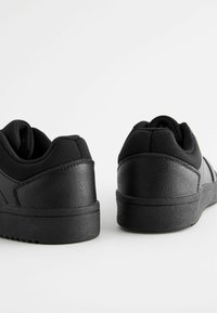 Des chaussures de sport noires avec une tige en cuir synthétique lisse et un col en textile rembourré. Dotées d'une semelle en caoutchouc plate et d'un design simple.
