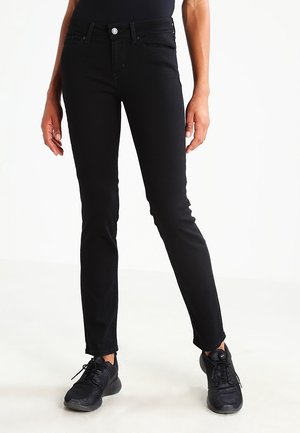 Jeans de mezclilla negros con un corte ajustado, que presentan un diseño estándar de cinco bolsillos y dobladillos deshilachados. Combinados con zapatillas deportivas negras.