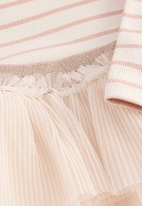 Gros plan sur un tissu rayé crème et rose avec une bordure dorée et un détail délicat de volants en tulle plissé.