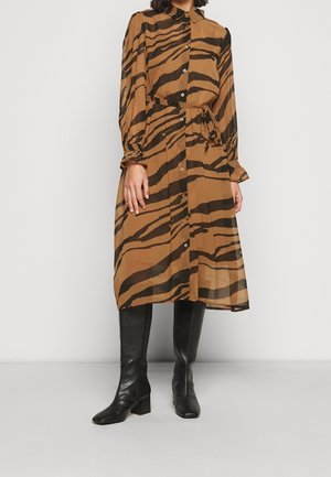Abito camicia a righe marroni e nere con maniche lunghe e risvolto, chiusura con bottoni e cintura in vita, abbinato a stivali neri con tacco al ginocchio.