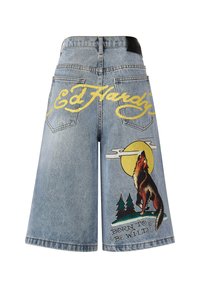 Pantalones cortos de mezclilla en azul claro con un logo amarillo en la parte trasera, gráficos de lobo y luna, y el texto "NACIDO PARA SER SALVAJE" en negro.