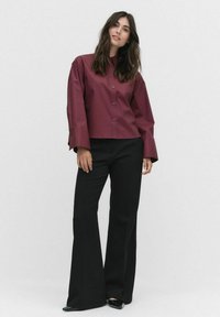 Bordeauxfarvet cropped button-up skjorte med brede ærmer, parret med sorte flared bukser og sorte sko. Glat tekstur og struktureret design.