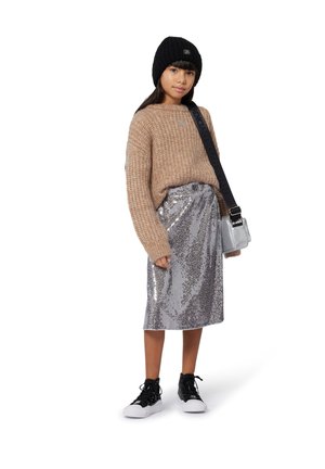 Young girl wearing a black knit beanie, beige sweater, silver sequin skirt, black high-top sneakers, and carrying a silver crossbody bag.