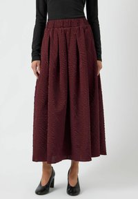 Bordeaux, struktureret midi-nederdel med elastisk talje, der har lodrette plisser og en flydende form. Satin nederdelen er parret med sorte hæle.