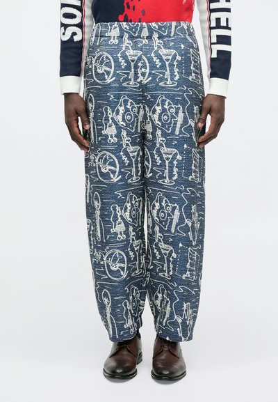 Μπλε παντελόνια με σχέδια που απεικονίζουν άσπρα γραφικά διάφορων αντικειμένων. Κατασκευασμένα από υφή υφάσματος με ελαστική μέση. Φοράει μαύρα παπούτσια.