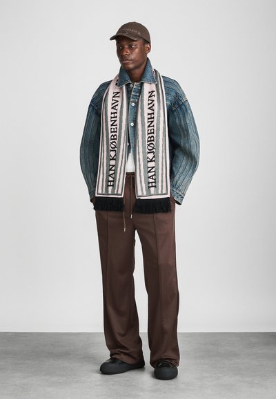 Chaqueta de mezclilla con rayas verticales, bufanda de punto con letras negras sobre fondo rosa, pantalones marrones y zapatos negros sin cordones.