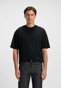 Black short-sleeve t-shirt in a loose fit with a crew neckline, made of smooth fabric. Paired with dark, textured denim pants.