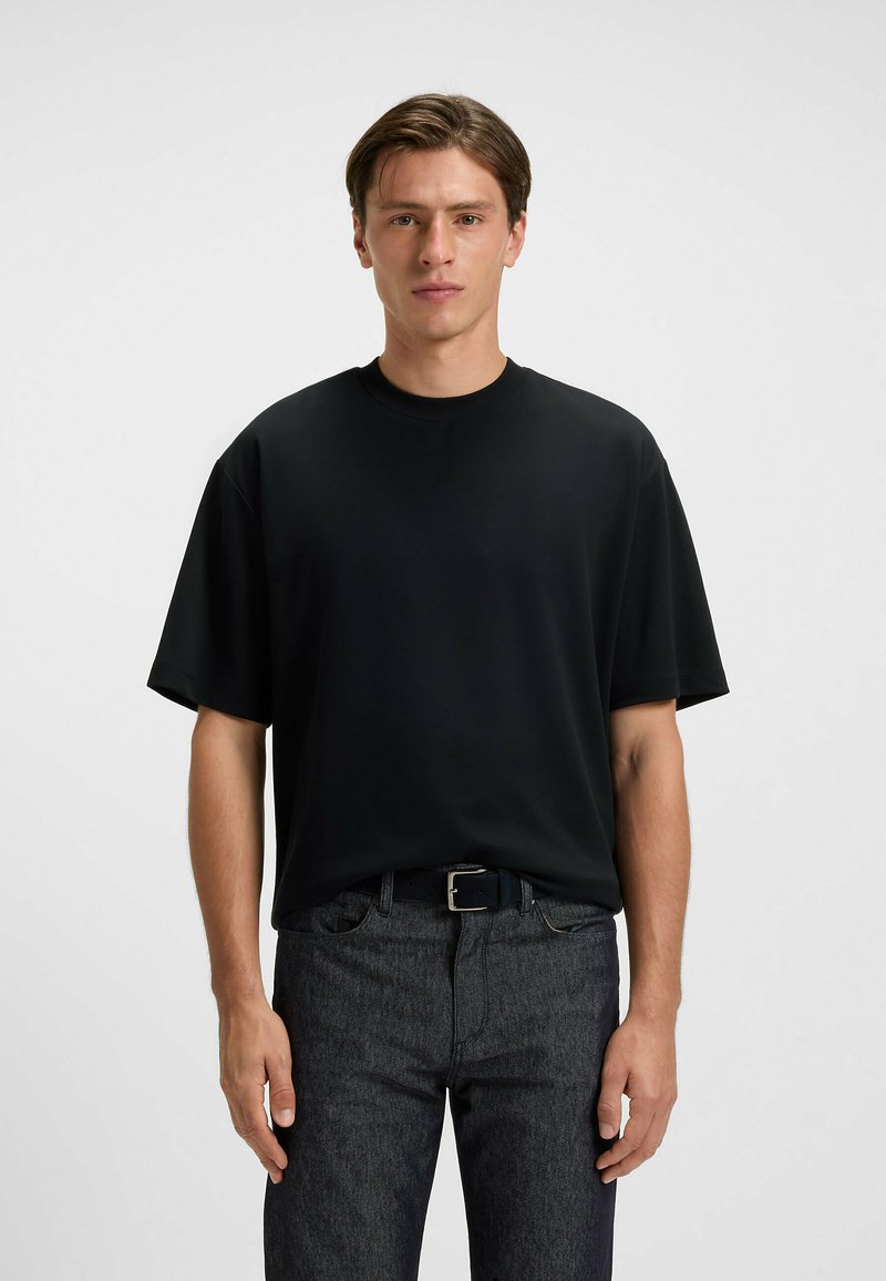 Black short-sleeve t-shirt in a loose fit with a crew neckline, made of smooth fabric. Paired with dark, textured denim pants.