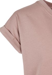 Ružové tričko s krátkym rukávom, zloženým manžetou a okrúhlym výstrihom, zobrazujúce detailnú štruktúru látky a švy.