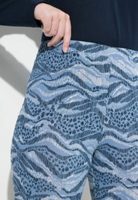 Blå mönstrade leggings med våg- och leopardtryck i ett texturerat tyg, med bred, elastisk midja och kontrasterande mörka detaljer.