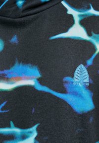 Svart stoff med et blått og grønt abstrakt mønster, med en liten brodert bladlogo i lyseblått nederst til høyre.
