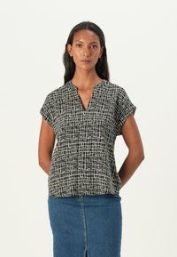 Black and white short-sleeve shirt with a V-neck, featuring a grid pattern. Lightweight fabric, structured fit, paired with a denim skirt.