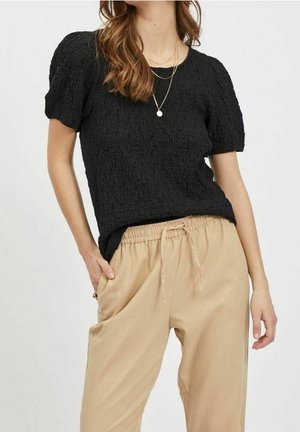 Maglietta nera con texture a maniche corte abbinata a pantaloni beige con vita elasticizzata, dotati di tasche laterali e una vestibilità rilassata.