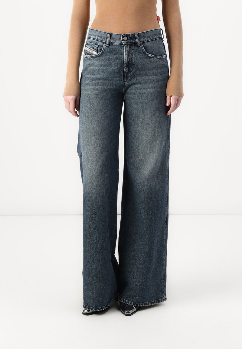 Weite Jeans aus dunkelblauem Denim mit Knopfleiste, fünf Taschen und subtilen Verfärbungen. Der Stoff hat eine glatte Textur und einen strukturierten Sitz.