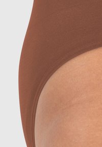 Bañador marrón con una textura suave, cinturilla elástica y corte curvado, mostrando un tono de piel adyacente al borde de la prenda.