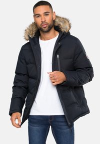Schwarze Puffjacke mit durchgehendem Reißverschluss, fellgefütterter Kapuze und Seitentaschen; verfügt über eine gesteppten Textur und elegantes Design.