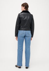 Black leather jacket with a soft black collar, fitted design, and button details. Paired with light blue, straight-leg jeans.