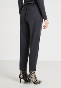 Pantalon gris foncé à coupe décontractée, ceinture élastique et poches latérales, associé à des bottines chelsea à imprimé serpent noir et or.