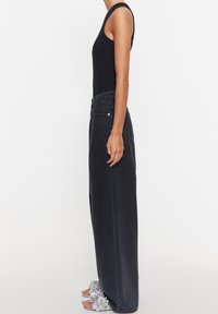 Musta ribbattu hihaton toppi yhdistettynä korkeavyötäröisiin, leveälahkeisiin mustiin farkkuihin. Farkuissa huomattavaa hopeaa metalliosissa. Remmi-sandaalit, joissa kukkakoristeita.