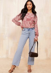 Maglietta lunga a maniche con motivo rosa e bianco, jeans larghi a vita alta blu chiaro e borsa a spalla marrone; abbinata a tacchi a strappo.