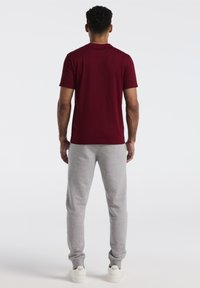 Burgunderfarbene Rundhals-T-Shirt kombiniert mit hellgrauen Sweatpants; das Outfit zeichnet sich durch einen lässigen Schnitt und weichen Baumwollstoff aus. Weiße Sneakers runden den Look ab.