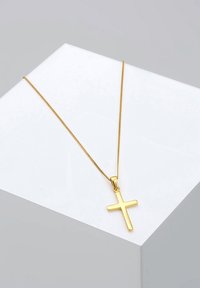 Guld kors vedhæng halskæde med en glat overflade, fastgjort til en tynd guldkæde, præsenteret mod en lysegrå geometrisk baggrund.