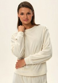 Biała, prążkowana bluzka z długim rękawem, z okrągłym dekoltem i marszczonymi mankietami. Tkanina ma miękką strukturę, co zapewnia luźny fason.
