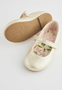 Bailarinas texturizadas en dorado con punta redonda, correa ajustable y plantilla con estampado floral. Suela de goma ligera con detalles en forma de estrella.