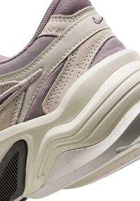 Primer plano del talón de una zapatilla beige y lila claro con suela en capas y detalles en cuero cosido y malla.